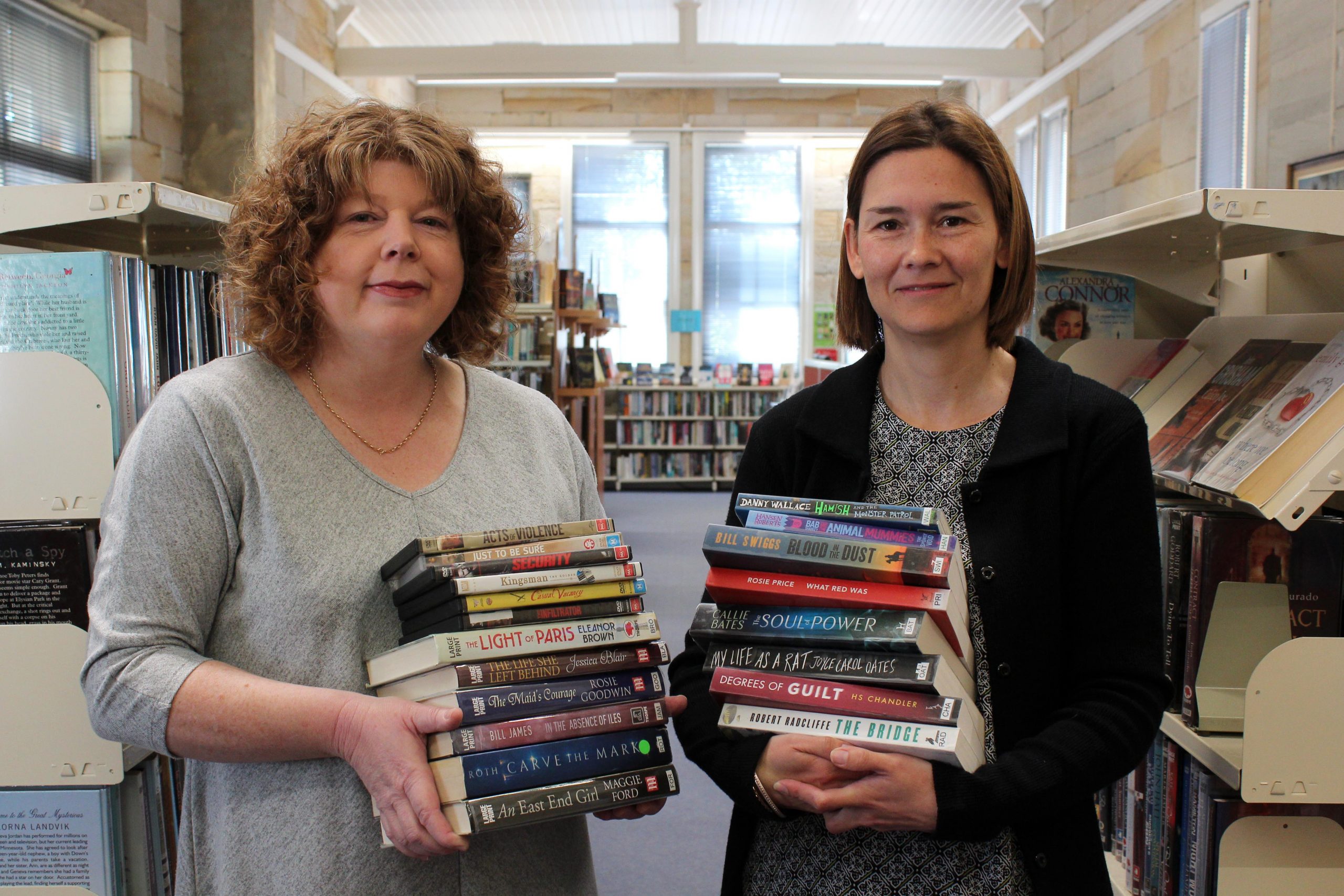 Two female librarians holding stacks of books inside library