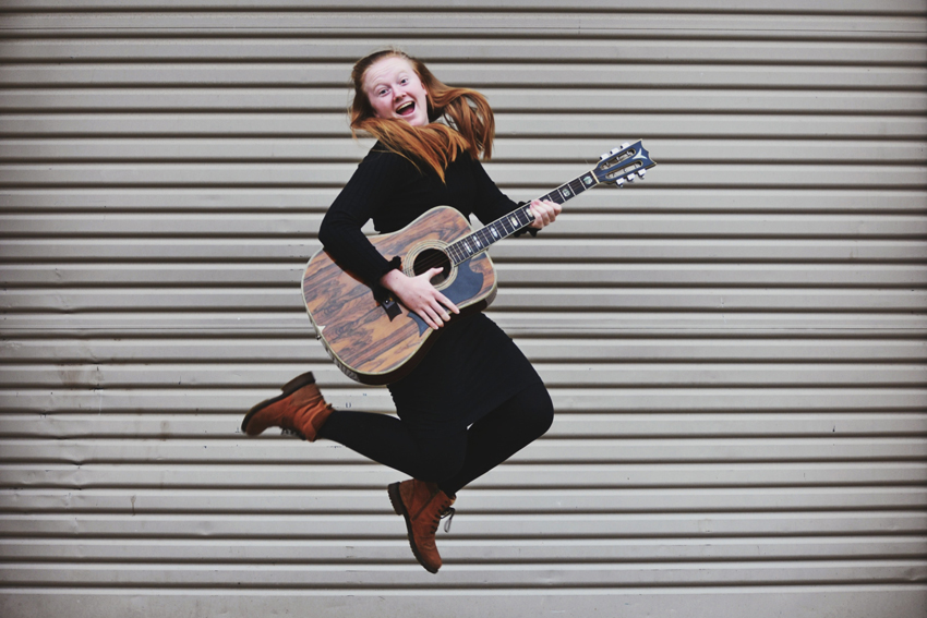 young girl with guitar jumping with joy