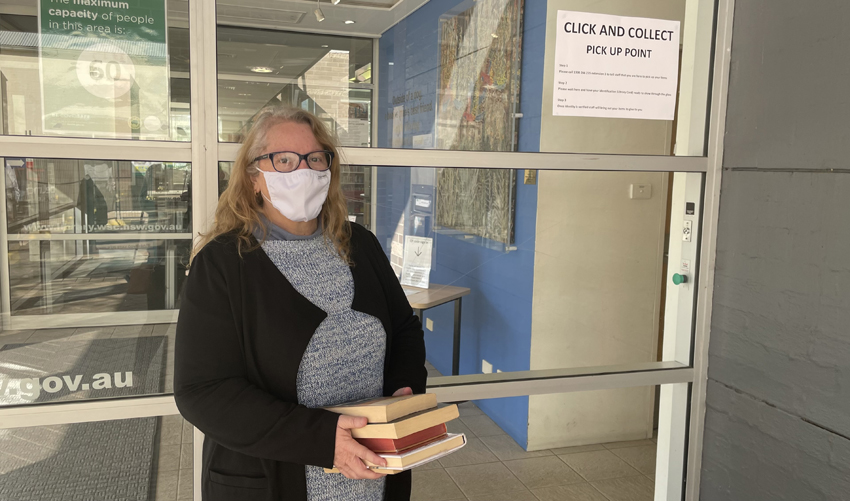 Librarian in face mask standing outside library, ready to hand over books to customer