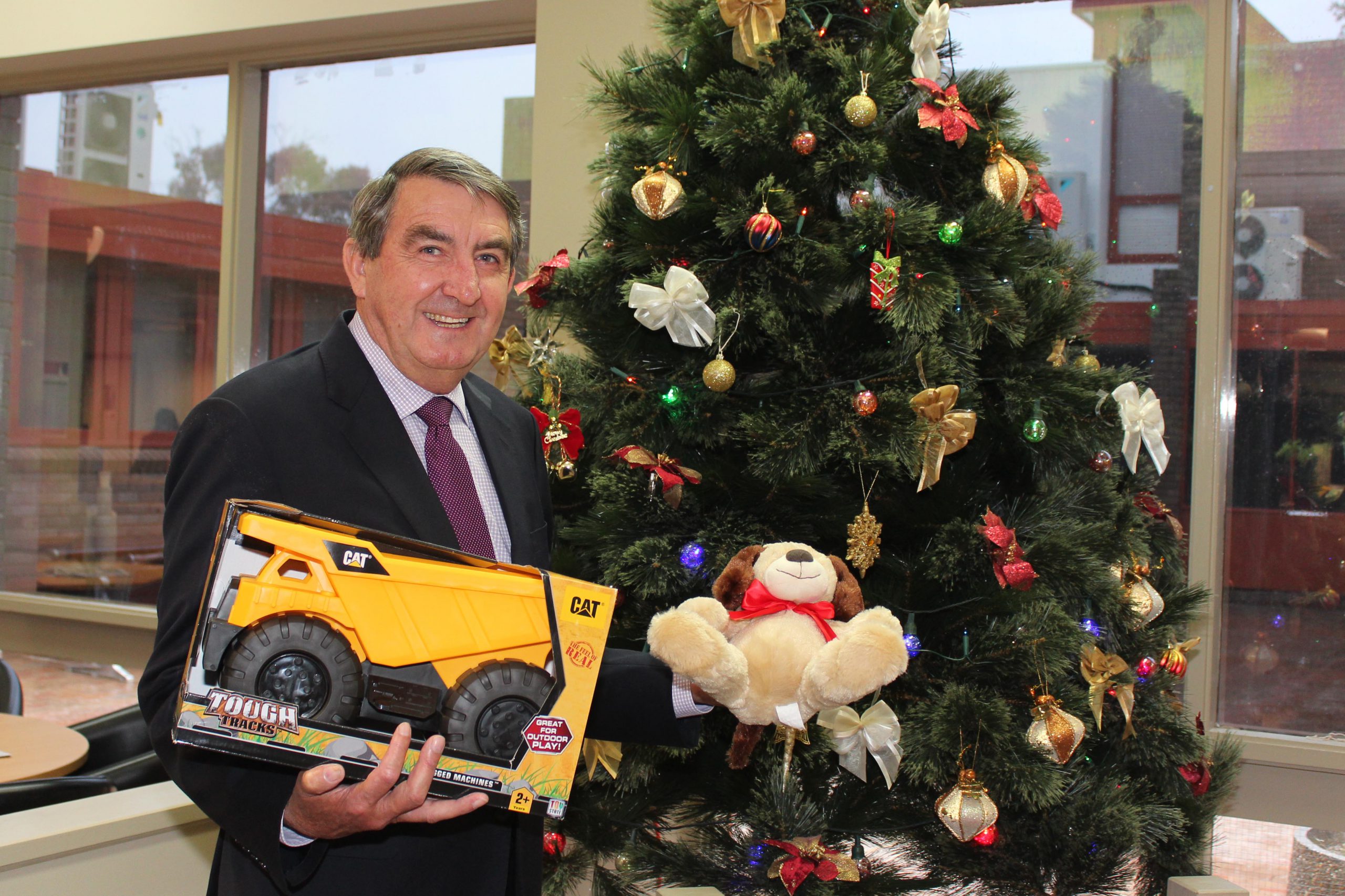 Mayor Duncan Gair holding gift in front of 2018 Christmas Giving Tree