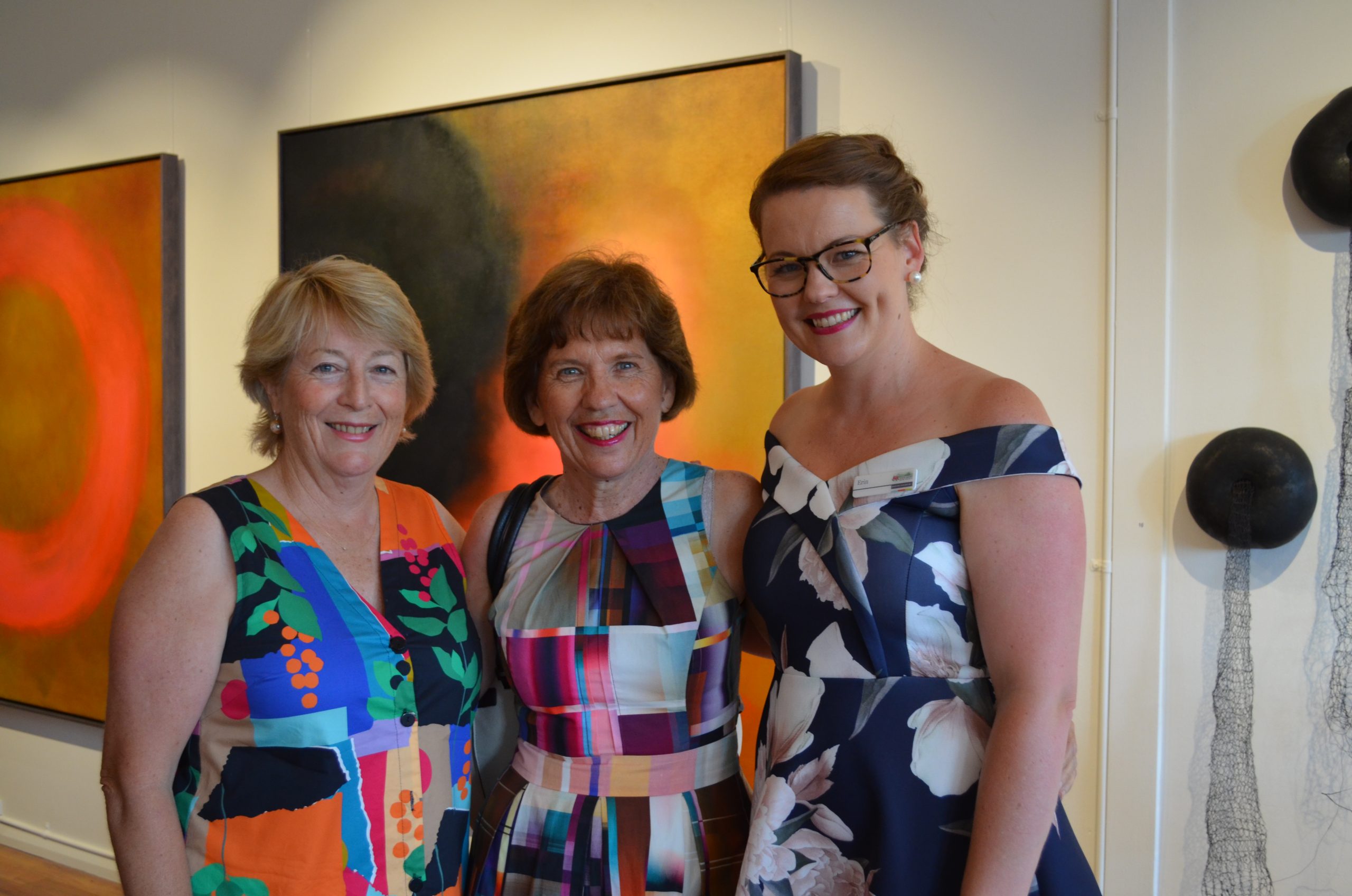 Three ladies smiling, standing in front of colourful abstract artwork