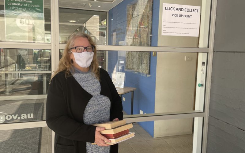 Librarian in face mask standing outside library, ready to hand over books to customer