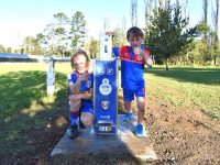 Two boys in soccer uniform standing next to water refill station on sunny day
