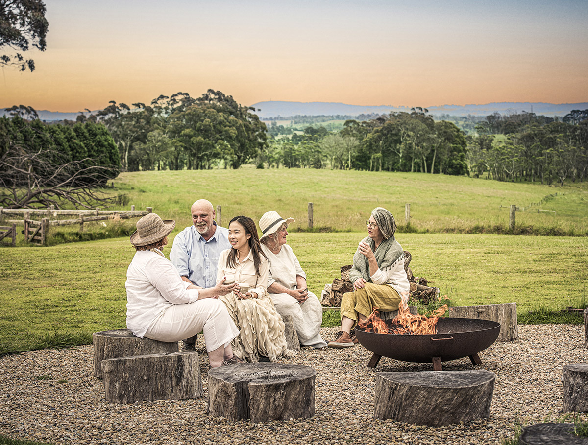People sitting around fire pit in rural setting at dusk