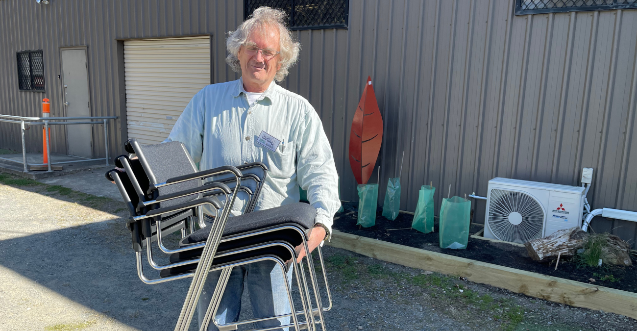 picture of mens shed member hoding up a stack of chairs